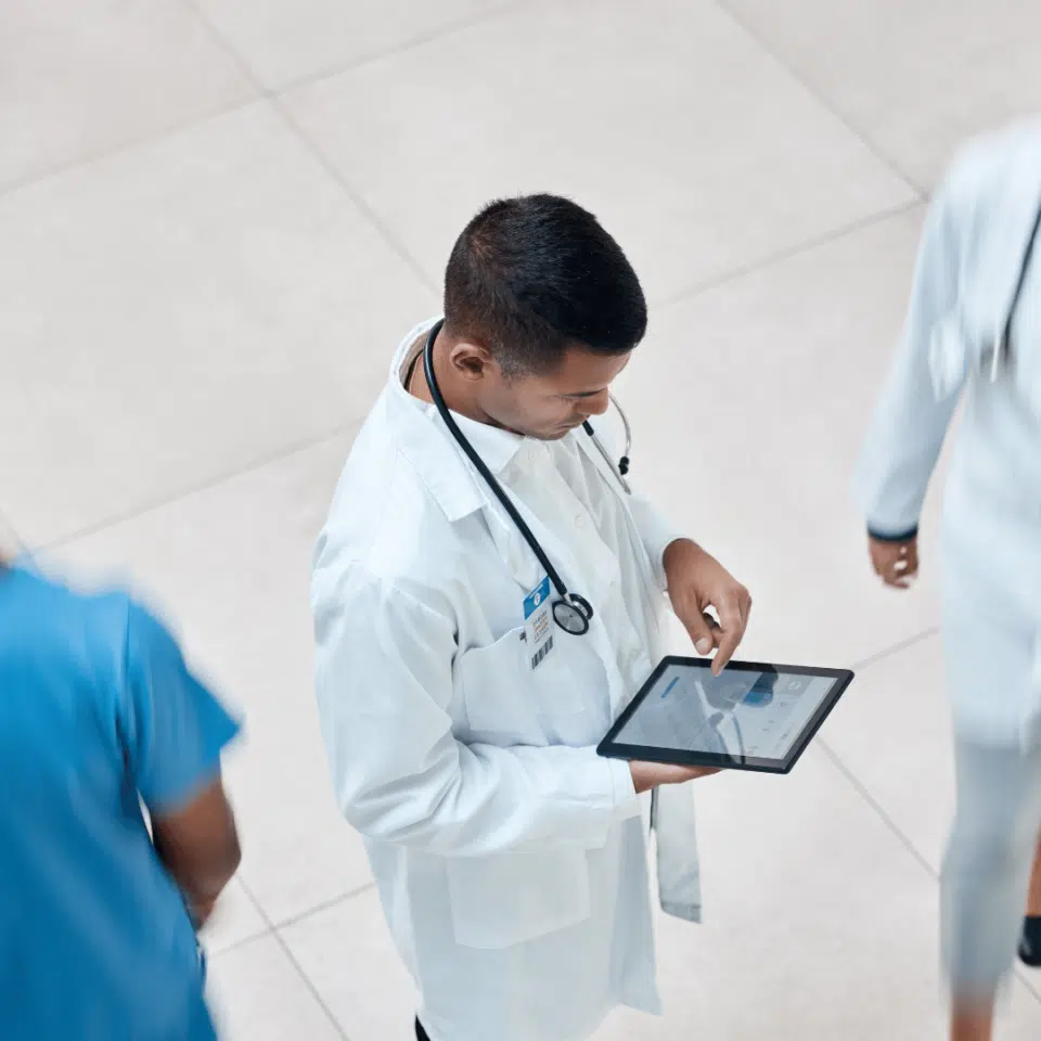 Médecin debout avec un stéthoscope autour du coup regardant une tablette dans ses mains vu du dessus