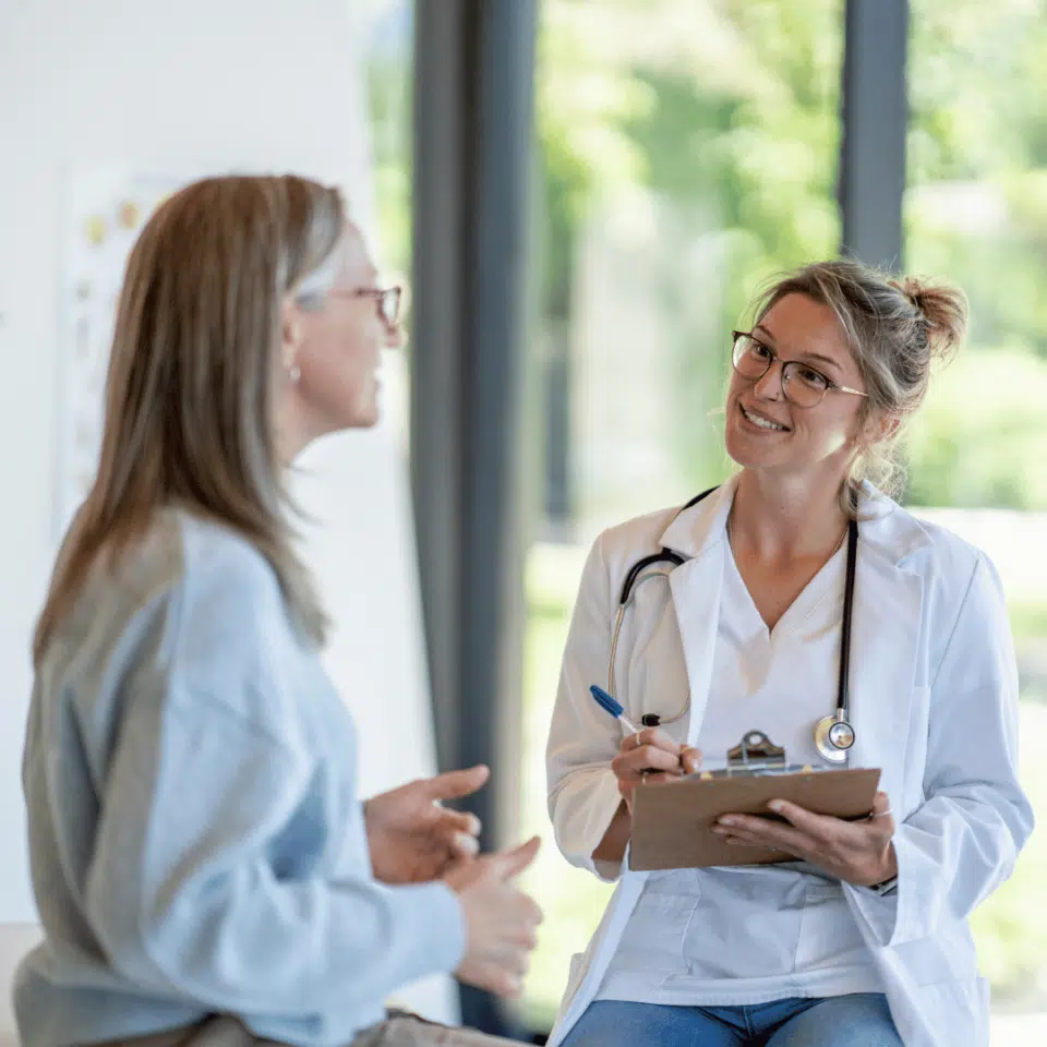 Professionnelle de santé avec un stéthoscope autour du cou écoutant sa patiente en prenant des notes
